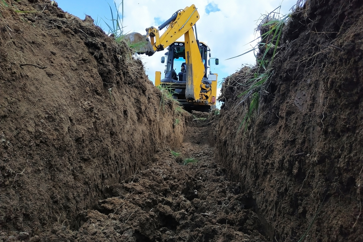 A yellow excavator digging a trench on the construction site, a close-up, against the sky.